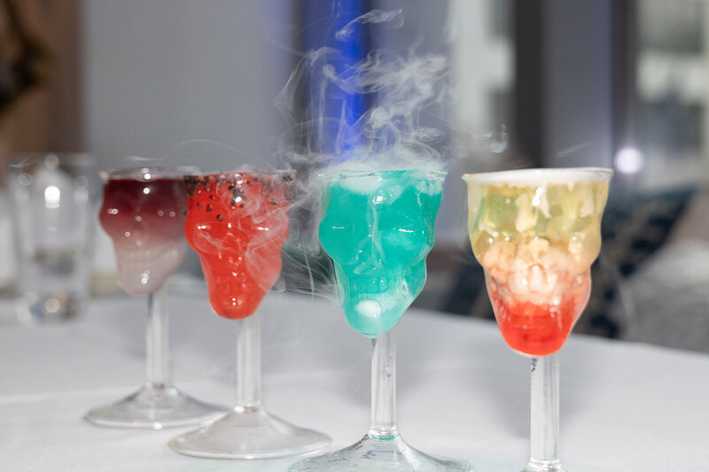 Four cocktails on bar top in skull shaped glasses
